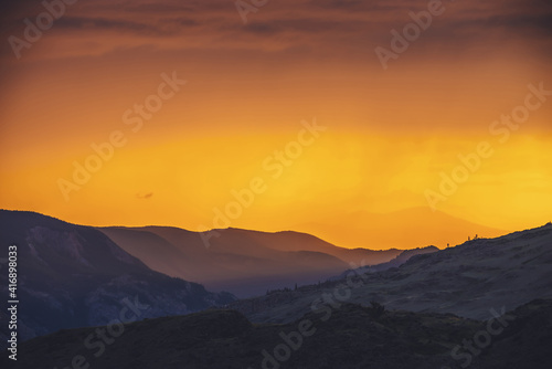 Atmospheric landscape with silhouettes of mountains and hills with trees on background of orange dawn sky. Colorful nature scenery with sunset or sunrise of illuminating color. Sundown paysage. © Daniil