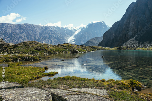 Sunny relaxing landscape with azure glacial lake in sunlight. Meditative ripple and glacier reflection on turquoise clear water of mountain lake. Beautiful scenery with lake and snowy mountains.