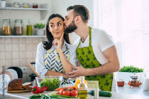 Excited smiling young couple in love making a super healthy vegan salad with many vegetables in the kitchen and having fun