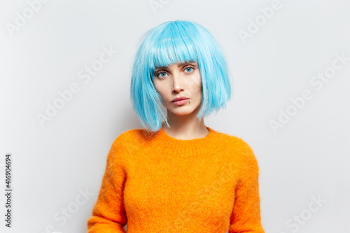 Studio portrait of young fashionable girl with blue hair in orange sweater against white background.