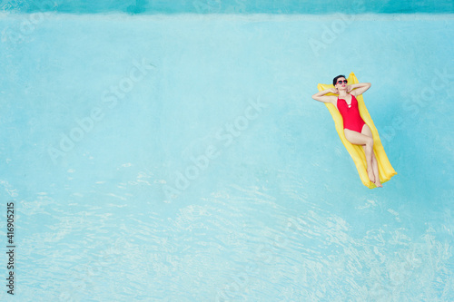 Enjoying suntan. Tropical vacation concept. Top view of young woman on the yellow air mattress in the swimming pool.