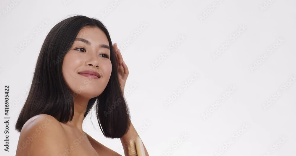 Young pretty asian woman brushing her hair with massage hairbrush and smiling, white background with empty space Young pretty asian woman brushing her hair with massage hairbrush and smiling, white background with empty space