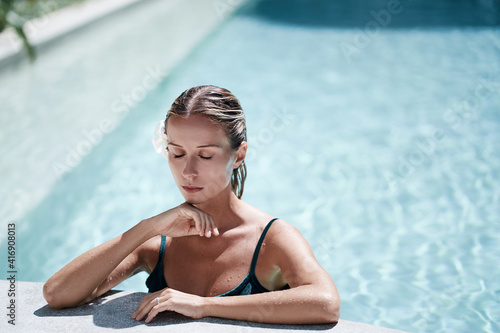 Enjoying suntan and vacation. Pretty young woman bathing in swimming pool.