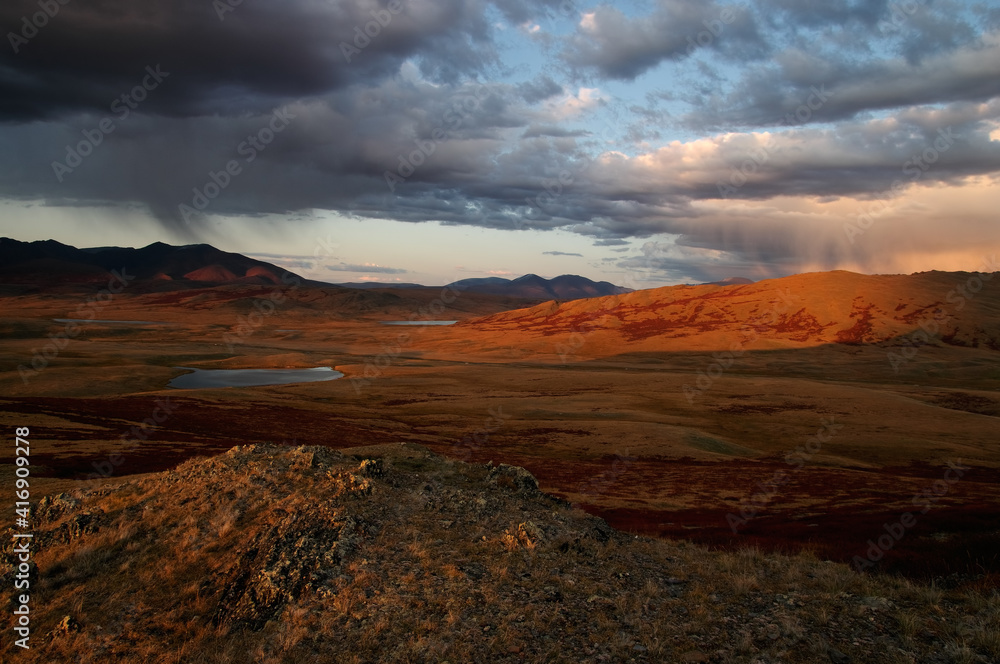 Dramatic sunset highland steppe valley with lakes with dry yellow grass on the background of rocky mountains under storm sky
