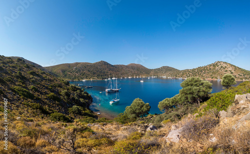 Summer sailing concept  A peaceful bay in the Aegean area with many moored yachts in tranquil waters on a sunny day. Turquoise blue sea with copy space. Green trees on bottom frame