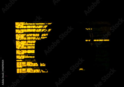 Silhouette of a hacker sitting in front of a monitor with yellow code in a dark room. Shallow depth of field. High quality photo