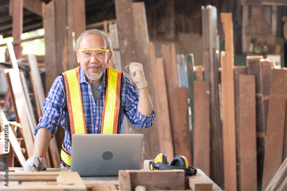 senior carpenter or worker looking at laptop computer excited by good news, celebrating success with arms raised senior carpenter or worker looking at laptop computer excited by good news, celebrating success with arms raised