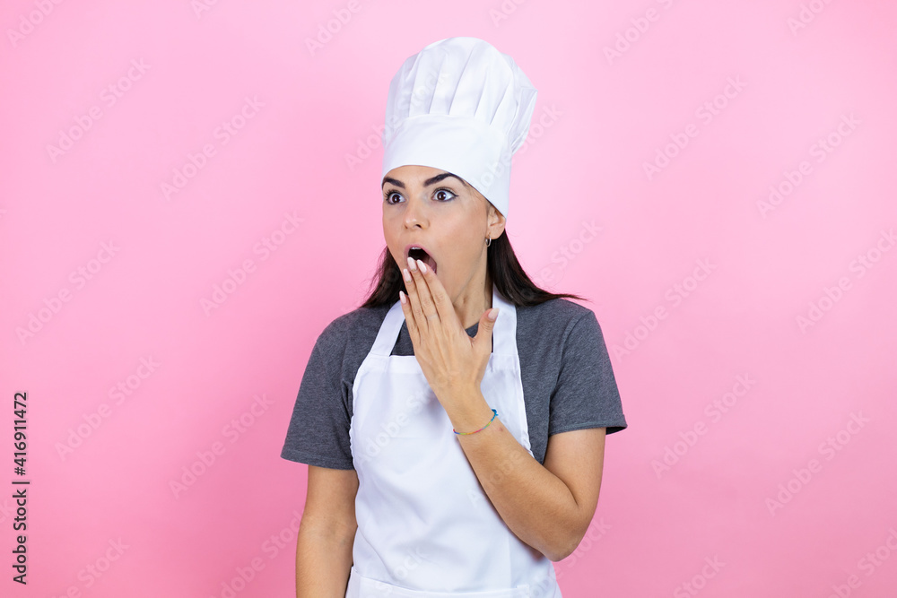 Young hispanic woman wearing baker uniform over pink background covering mouth with hand, shocked and afraid for mistake. surprised expression Young hispanic woman wearing baker uniform over pink background covering mouth with hand, shocked and afraid for mistake. surprised expression