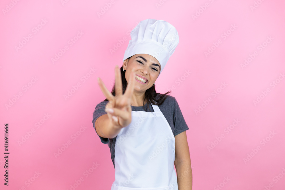 Young hispanic woman wearing baker uniform over pink background showing and pointing up with fingers number three while smiling confident and happy Young hispanic woman wearing baker uniform over pink background showing and pointing up with fingers number three while smiling confident and happy