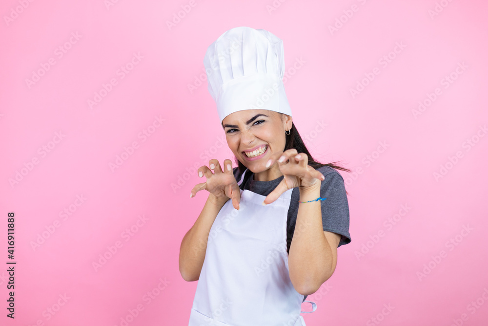Young hispanic woman wearing baker uniform over pink background smiling funny doing claw gesture as cat, aggressive and sexy expression Young hispanic woman wearing baker uniform over pink background smiling funny doing claw gesture as cat, aggressive and sexy expression