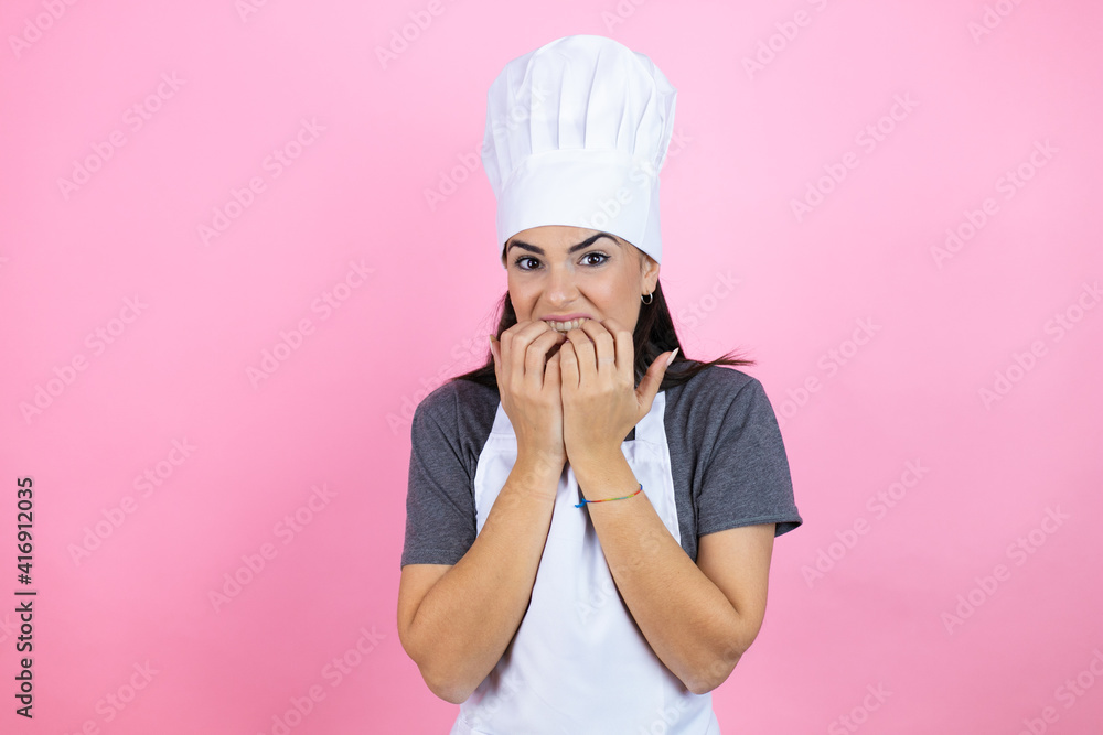 Young hispanic woman wearing baker uniform over pink background looking stressed and nervous with hands on mouth biting nails. anxiety problem. Young hispanic woman wearing baker uniform over pink background looking stressed and nervous with hands on mouth biting nails. anxiety problem.