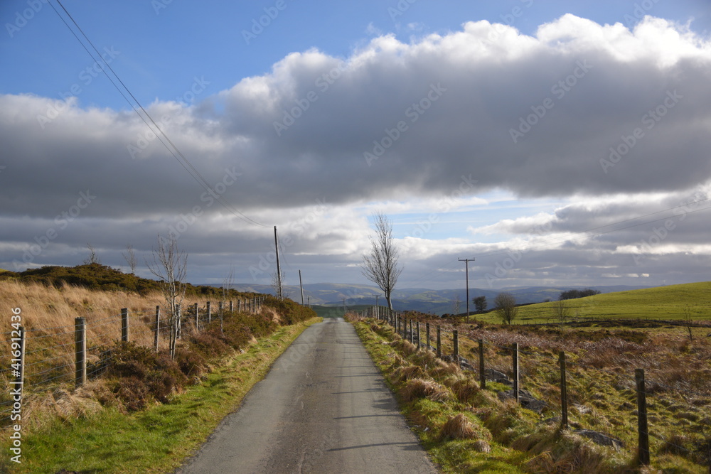 a small road that leads to llyn marw near caersws in wales, surrounded by fields and barbed fences