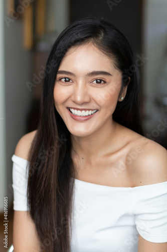 Young Asian teenage girl on white background. Casual Asian woman wearing white t-shirt posing to the camera at home. Portrait of casual Asian woman smiling indoor.