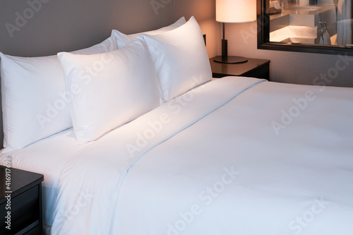 Clean Bedding sheets and pillow on natural wall room background. White bedding and pillow in hotel room. White pillows on empty bed.