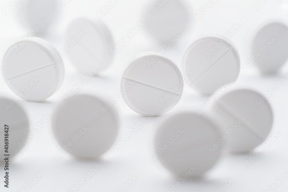 A pile of white pills scattered on a bright white background. Selective focus.