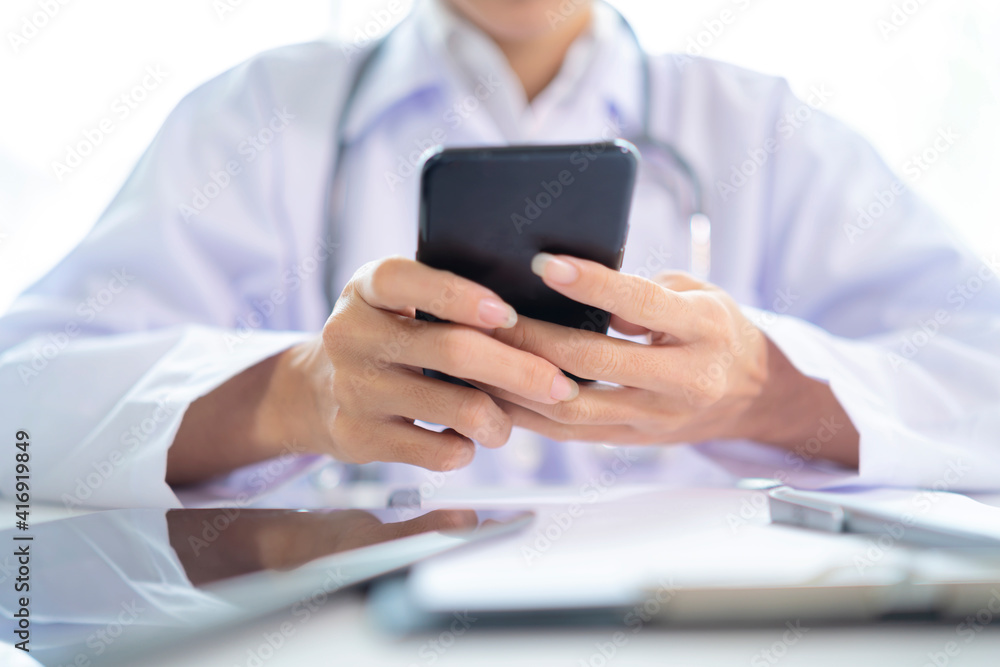 Female doctor hands holding and using mobile smart phone with laptop computer and stethoscope on the table Female doctor hands holding and using mobile smart phone with laptop computer and stethoscope on the table