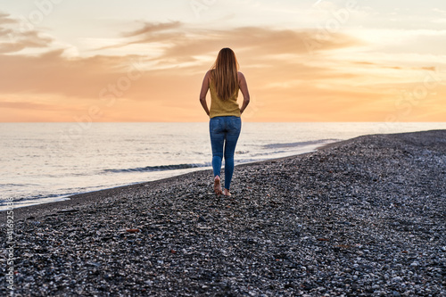 Young woman alone walking on the beach sand at sunset. Concept of relaxation and meditation