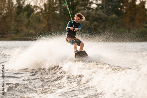 Beautiful view of man holding bright cable and balancing on wakeboard on wave.