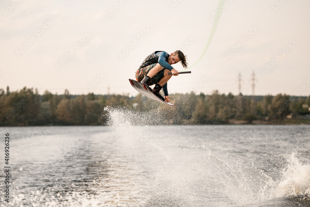athletic man with bent knees jumps on wakeboard over the water
