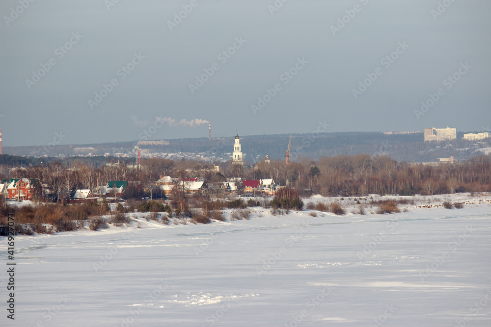 Naklejka premium A small settlement with a towering bell tower on the bank of a frozen river.