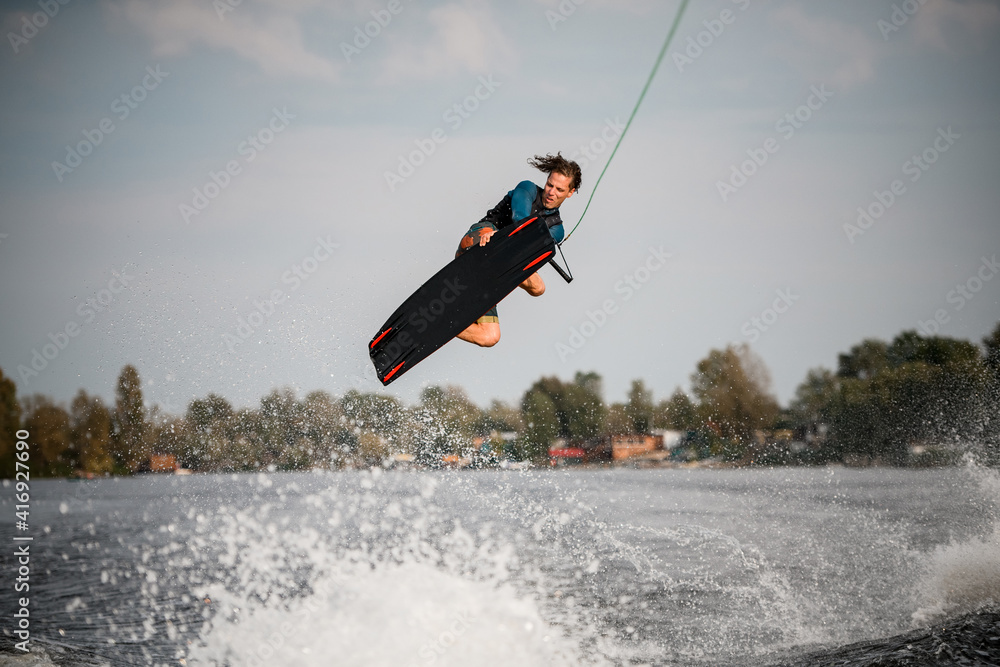 young man on wakeboard spectacularly jumps and performs tricks over the water.