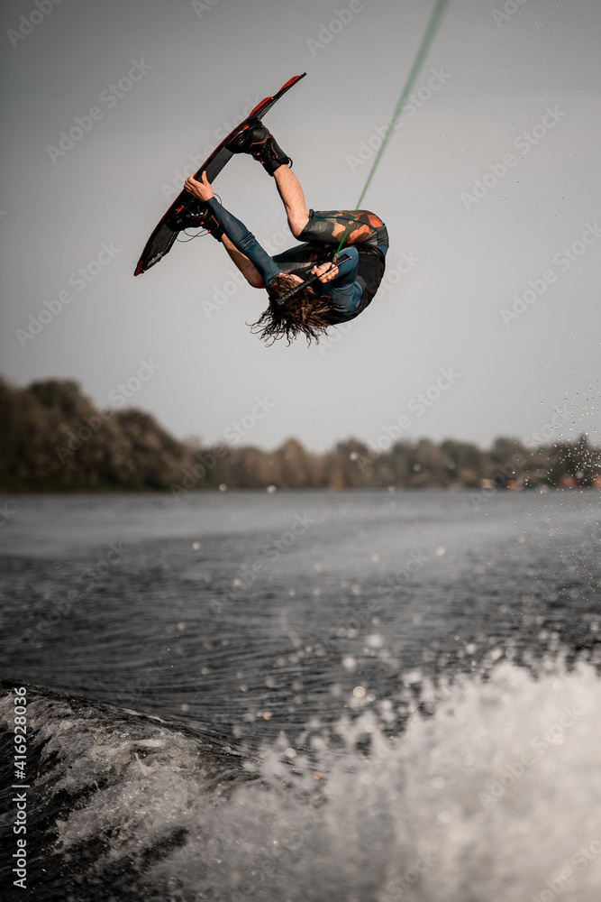 active man doing extreme high jump on wakeboard over splashing river wave