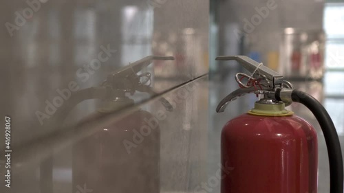 Close-up on Fire extinguisher in modern building. The lens shakes slightly. Tilt shot from top to bottom. The subject is on the right.