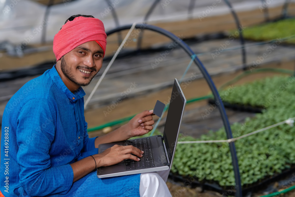 Young indian farmer using laptop at greenhouse or poly house