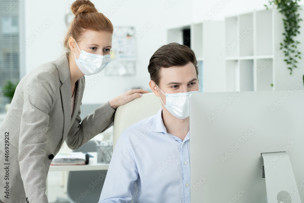 Young colleagues in protective masks and formalwear looking at computer screen Young colleagues in protective masks and formalwear looking at computer screen