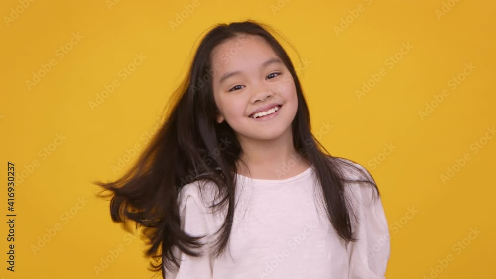 Cute cheerful asian girl shaking her hair and smiling at camera, orange studio background Cute cheerful asian girl shaking her hair and smiling at camera, orange studio background