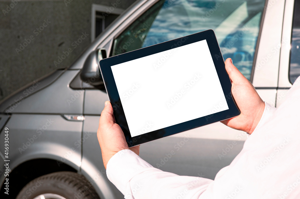 Mock up technology. Businessman in a white shirt holds a tablet with a white screen on the background of a minibus.