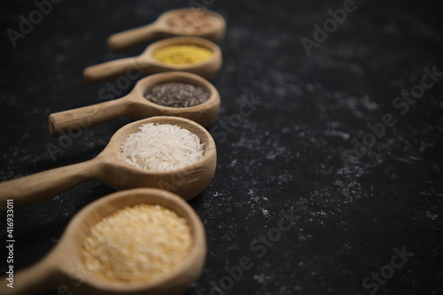 Spices. Chia seeds, millet, rice, chickpeas, quinoa in a wooden spoon on a black and gray background. Five spoons in a row. Selective soft focus