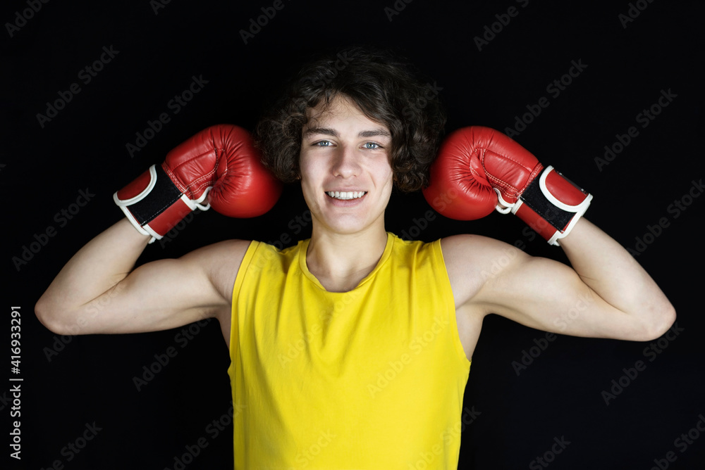 Young boxer - a teenage guy on a dark background in boxing gloves shows how strong and agile he is. A guy with a beautiful smile and boxing gloves, learning to protect himself Young boxer - a teenage guy on a dark background in boxing gloves shows how strong and agile he is. A guy with a beautiful smile and boxing gloves, learning to protect himself