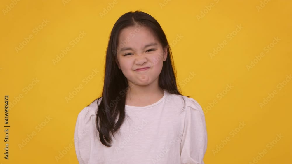 Little asian girl shaking her head in denial and frowing her face, orange studio background, slow motion Little asian girl shaking her head in denial and frowing her face, orange studio background, slow motion
