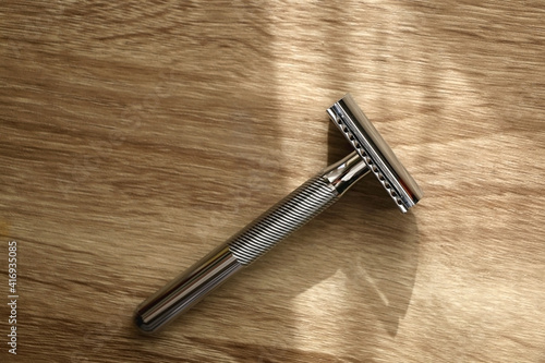 Reusable metal safety razor on wooden background. Selective focus.