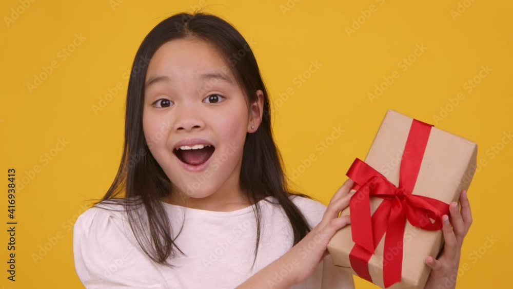 Emotional happy asian girl enjoying gift, looking at box with excitement, orange studio background, slow motion Emotional happy asian girl enjoying gift, looking at box with excitement, orange studio background, slow motion