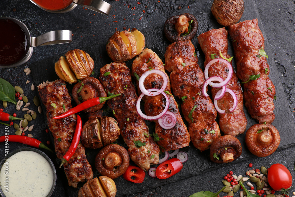 Assorted fried meat and grilled vegetables. Shish kebab, lula, potatoes, mushrooms with sauce on a black board on table.Fresh tomatoes, chili peppers, onions, herbs and spices. Background, top view Assorted fried meat and grilled vegetables. Shish kebab, lula, potatoes, mushrooms with sauce on a black board on table.Fresh tomatoes, chili peppers, onions, herbs and spices. Background, top view