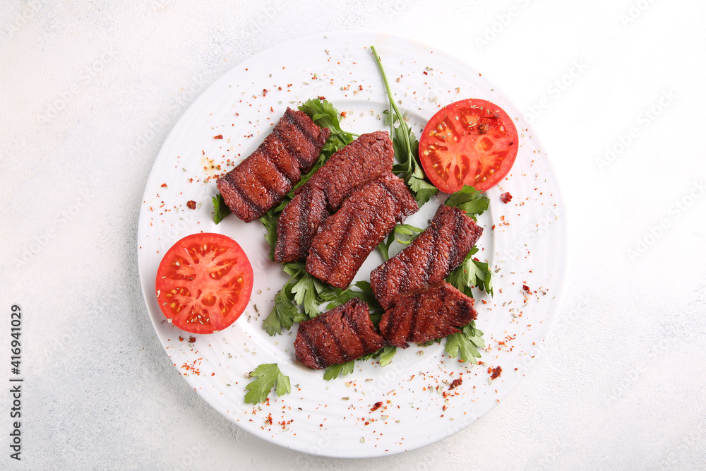 Slices of roast meat with spices, herbs and tomatoes on a white plate on a white table. Restaurant menu, background image, copy space, top view, horizontal. Fried beef