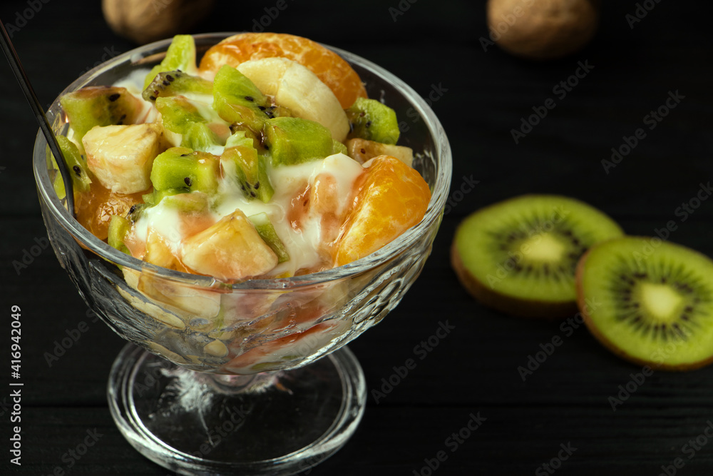 fruit salad in a glass bowl. Kiwi, banana and tangerine with yoghurt and fruit topping. A healthy, vitamin-rich snack. Healthy nutrition concept. Black wood background. High quality photo fruit salad in a glass bowl. Kiwi, banana and tangerine with yoghurt and fruit topping. A healthy, vitamin-rich snack. Healthy nutrition concept. Black wood background. High quality photo