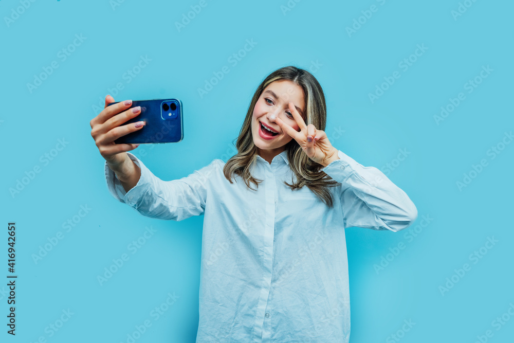 Time for a selfie. Studio photo on blue background of smiling girl taking selfie on modern smartphone, place for text Time for a selfie. Studio photo on blue background of smiling girl taking selfie on modern smartphone, place for text