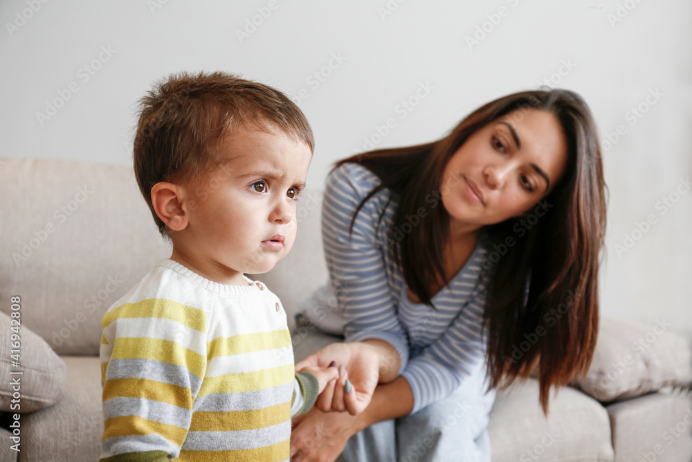 Portrait of adorable little boy sitting on the textile couch with his mom and crying. Upset toddler throwing a tantrum at home. Barefoot calling for attention. Close up, copy space, background. Portrait of adorable little boy sitting on the textile couch with his mom and crying. Upset toddler throwing a tantrum at home. Barefoot calling for attention. Close up, copy space, background.