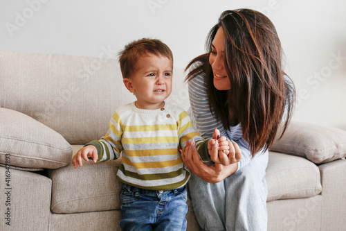 Portrait of adorable little boy sitting on the textile couch with his mom and crying. Upset toddler throwing a tantrum at home. Barefoot calling for attention. Close up, copy space, background. photo