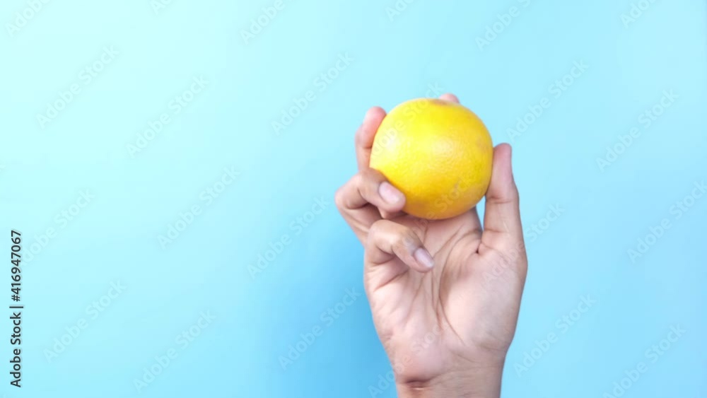 close up of person hand holding a orange against a blue background close up of person hand holding a orange against a blue background
