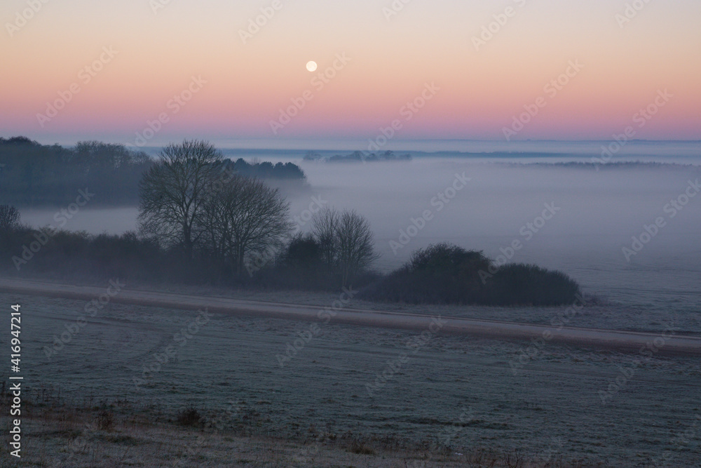 an early morning mist filled valley with the snow moon low in the sunrise sky an early morning mist filled valley with the snow moon low in the sunrise sky