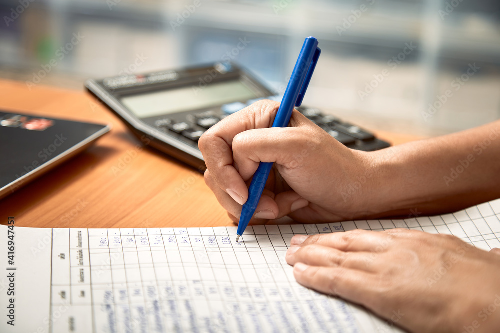 Fototapeta premium Close up view female hand holding pen taking notes of expenses in the budget book.