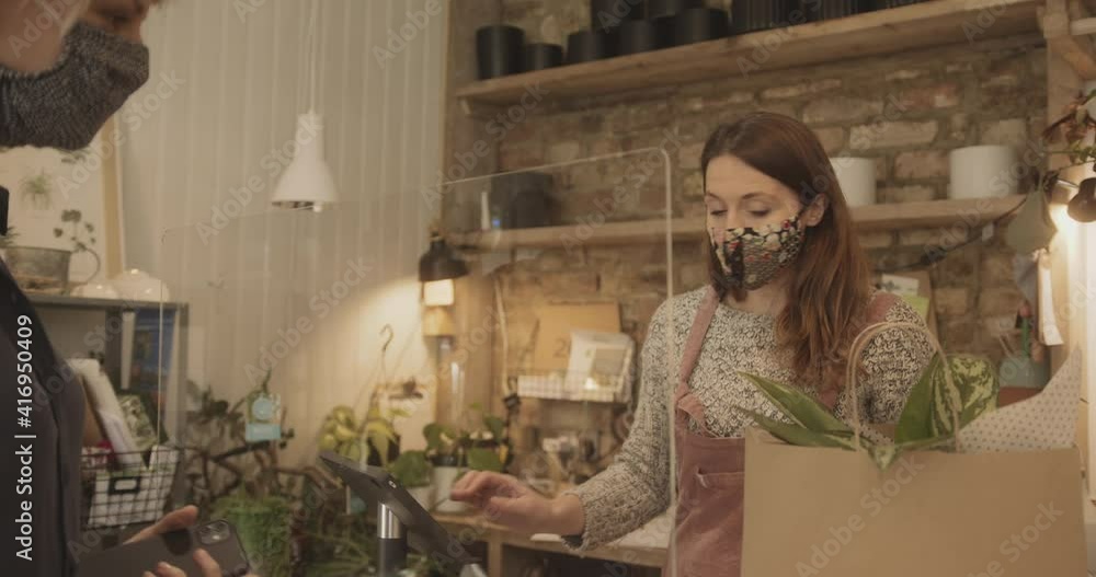 Retail clerk wearing face mask giving shopping bag to customer in store after contactless payment Retail clerk wearing face mask giving shopping bag to customer in store after contactless payment