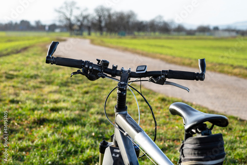 A bicycle handlebar seen from the first person perspective. Visible bicycle frame and bicycle accessories on the handlebar, and the road in the background.