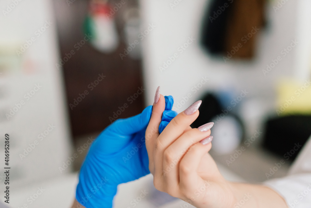 Manicurist wearing protective mask painting female nails with nail polish in a manicure salon.