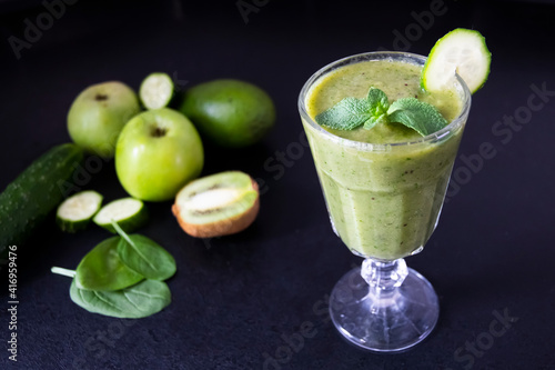 Delicious green smoothie and fresh fruits on black table. Healthy green smoothie with banana, spinach, avocado, apple and mint in a glass. Vegan food.