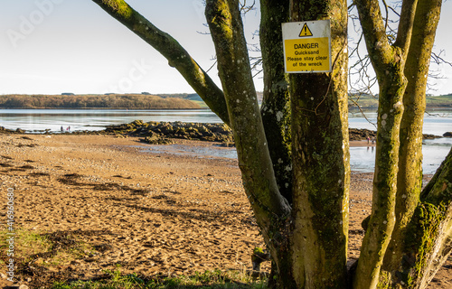 Danger Quicksand, please say clear of the wreck sign on a tree beside a beach photo